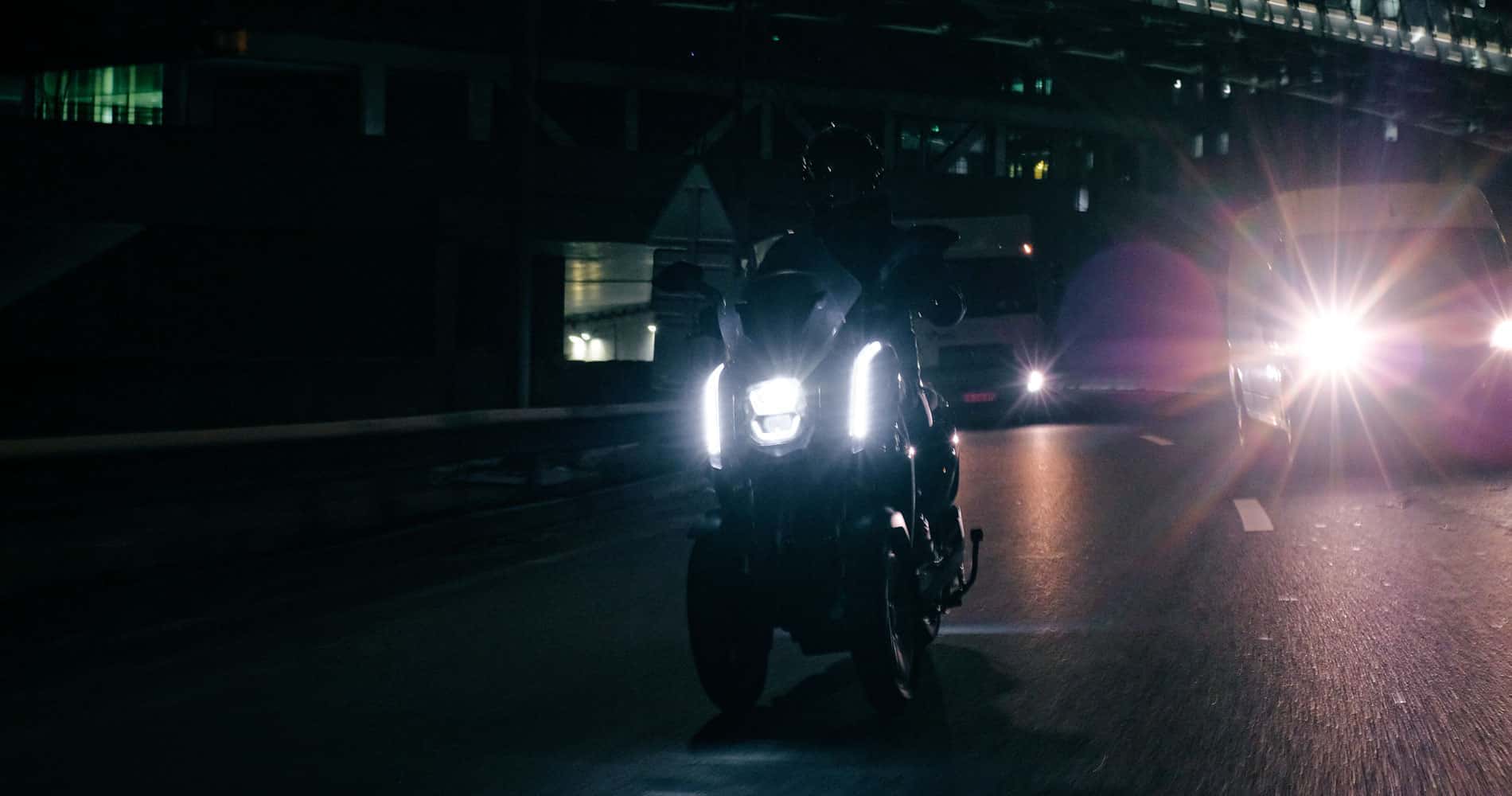 Un scooter 3 roues électrique roulant dans Paris de nuit