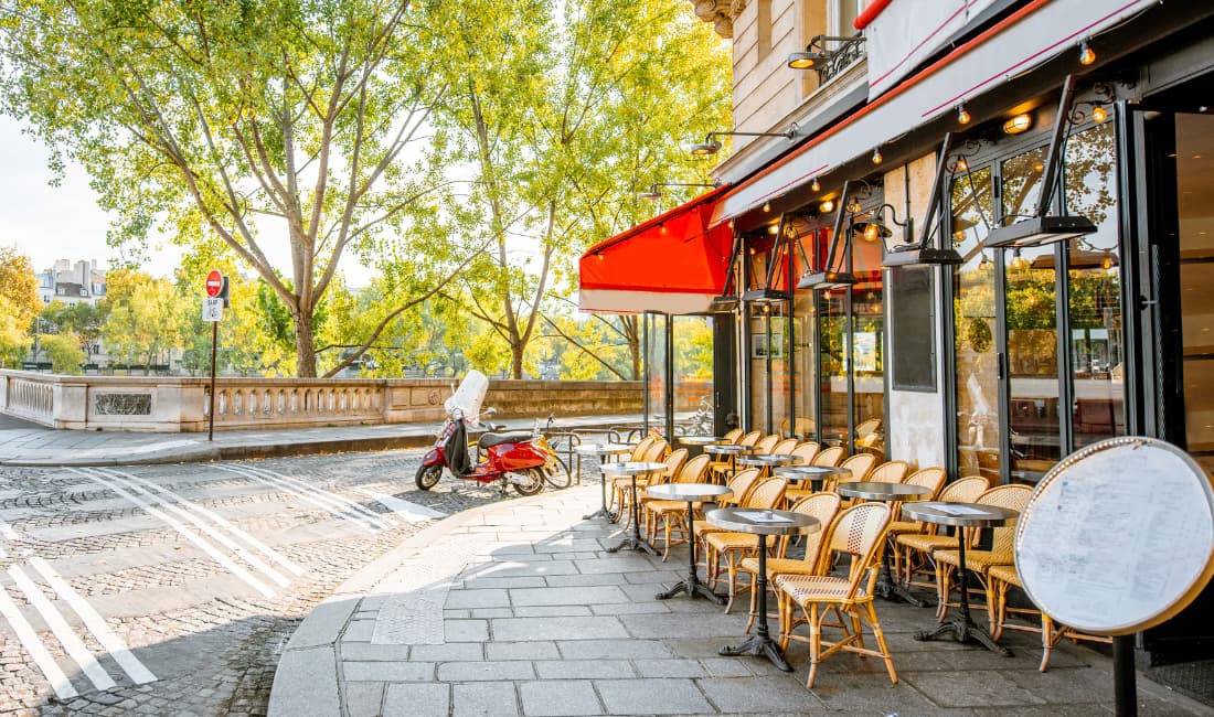 Au soleil, la terrasse d'un café de Paris avec un petit parking pour scooter devant